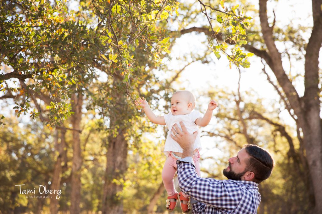 dad lifting his daughter up to reach a leave on a tree