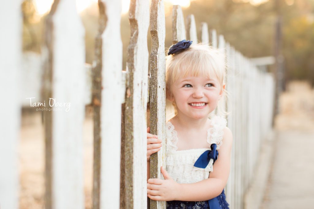 little girl smiling near a white fence