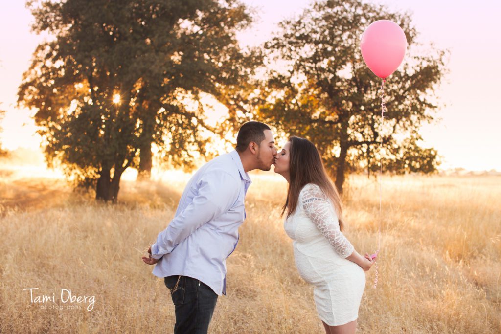 pregnant mom kissing expecting dad with pink balloon behind her back