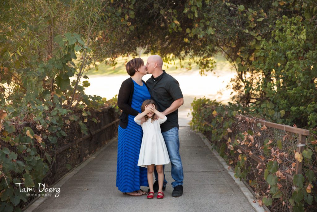 couple kissing with daughter covering her eyes