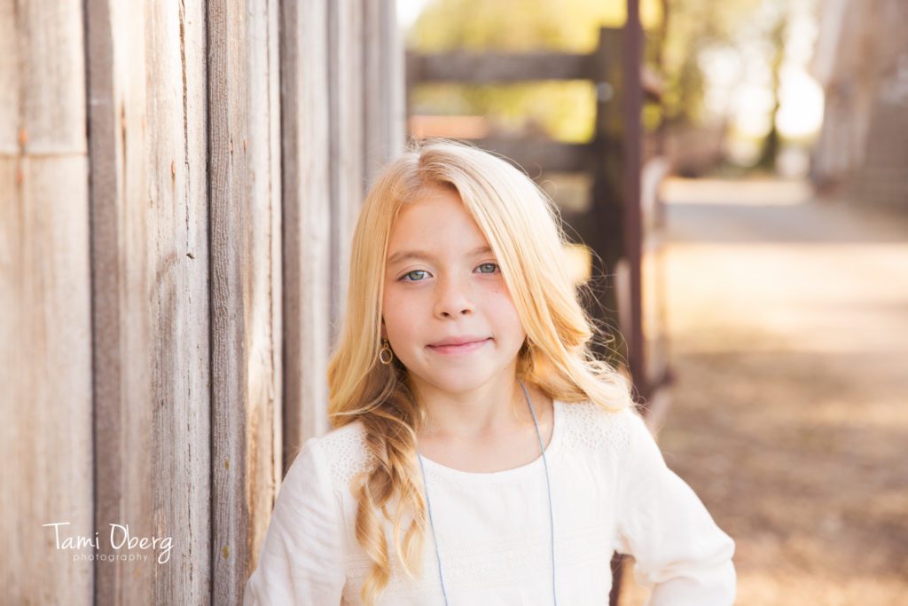 6 year old girl leaning against an old barn